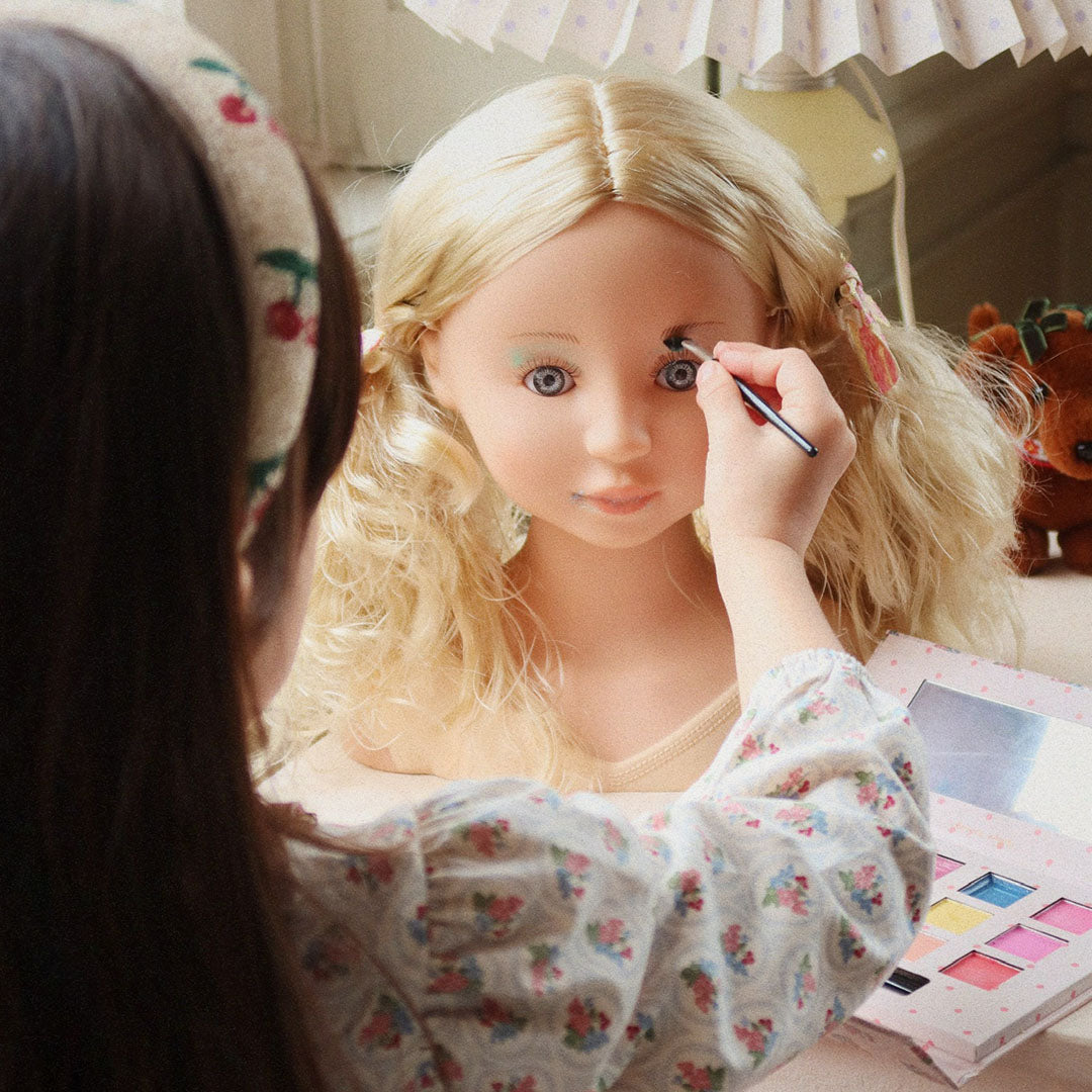 Een kind schminkt de Konges Sløjd make-up pop Lili met een kwastje uit het make-up palet.