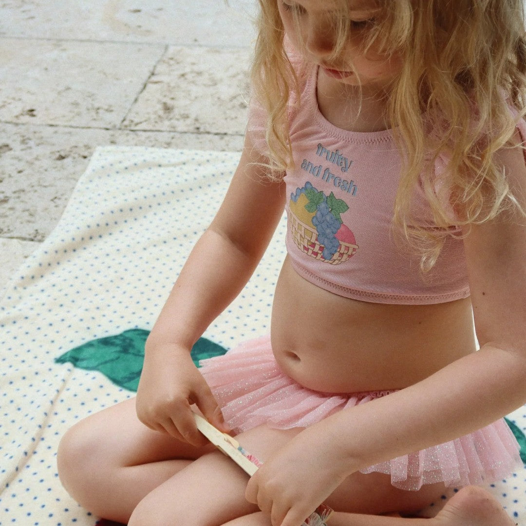 Een kind zit op het Konges Sløjd strandlaken met kersenprint en stippen.