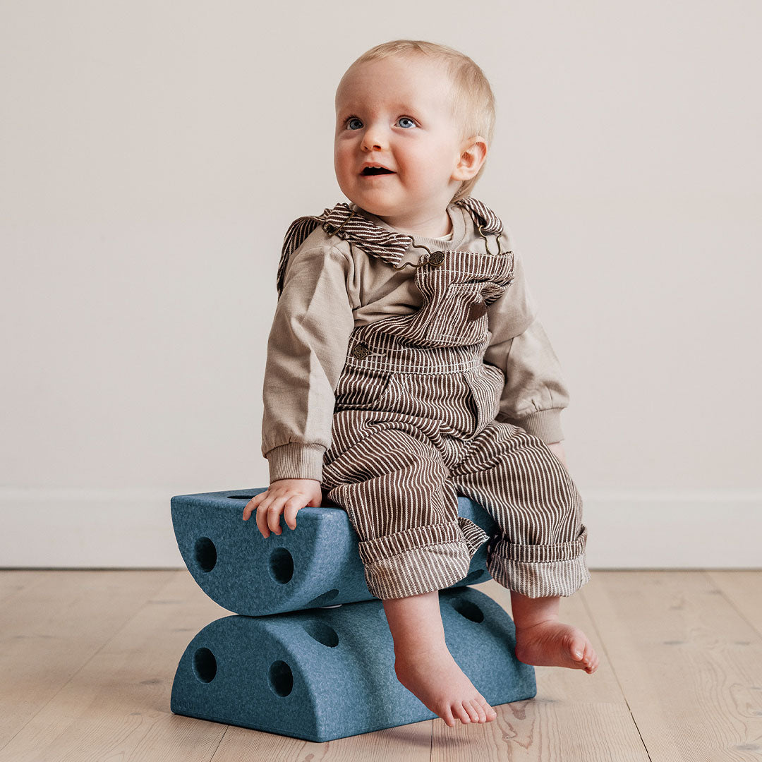 Baby zit op twee gestapelde Modu blauwe halfronde schuimrubberblokken.