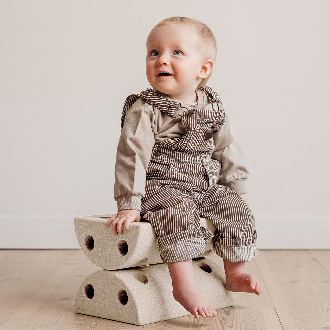 Baby zit op twee gestapelde Modu halfronde beige schuimrubber blokken.