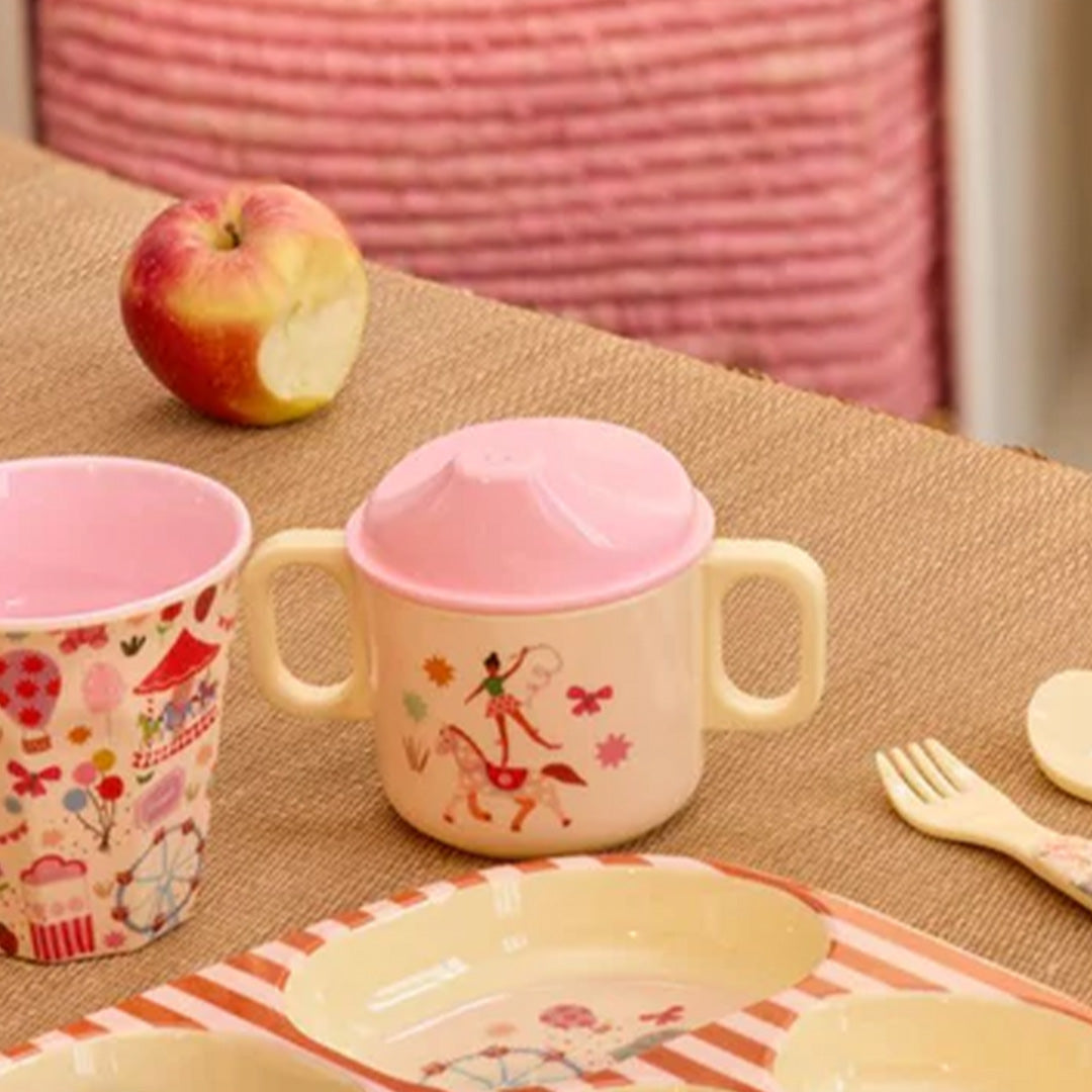 De Rice tuitbeker staat op een tafel met ander kinderservies en een appel.