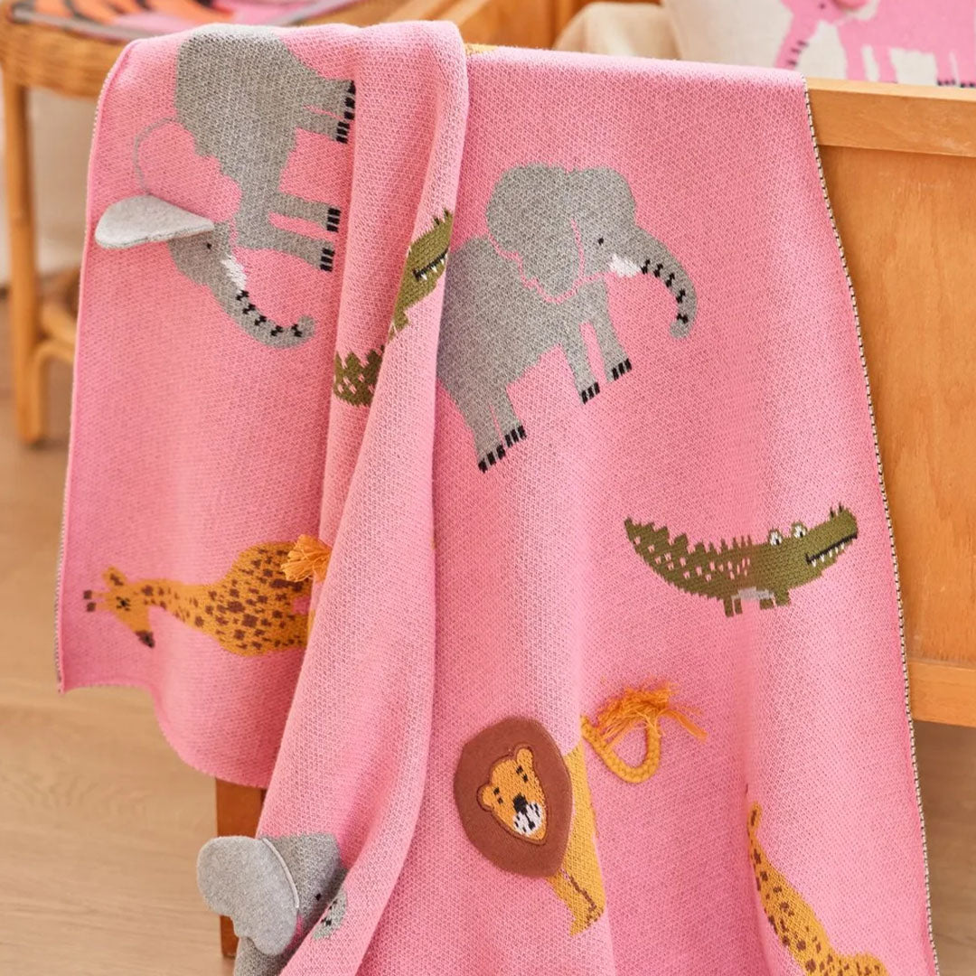 Roze rice babydeken met savanne dieren, gedrapeerd over een houten ledikant.