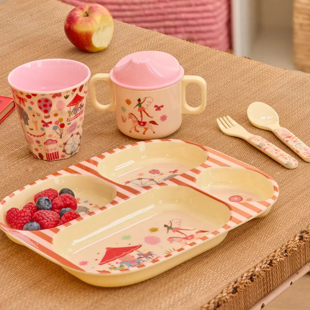 rice vakjesbord met fun fair thema, gevuld met fruit, samen met een bijpassende beker, tuitbeker en bestekset op een tafel.