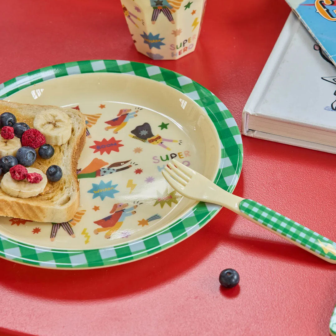 rice kinderbord met superheldenfiguren en een boterham met fruit op een rode tafel, met een bijpassende vork.