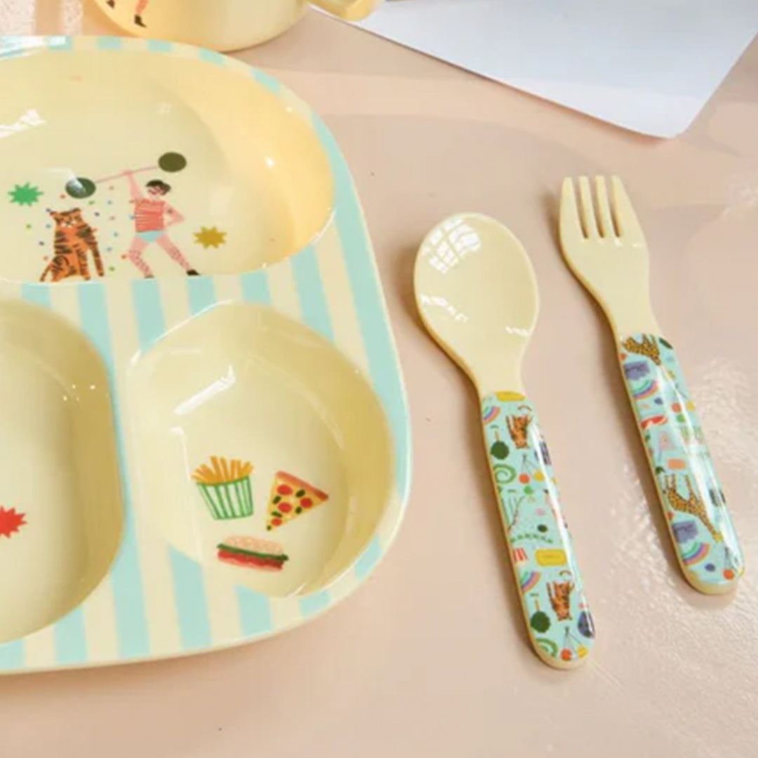 Rice kinderbestek set met lepel en vork met mintgroene handvatten, liggend naast een geel-blauw gestreept kinderbord.