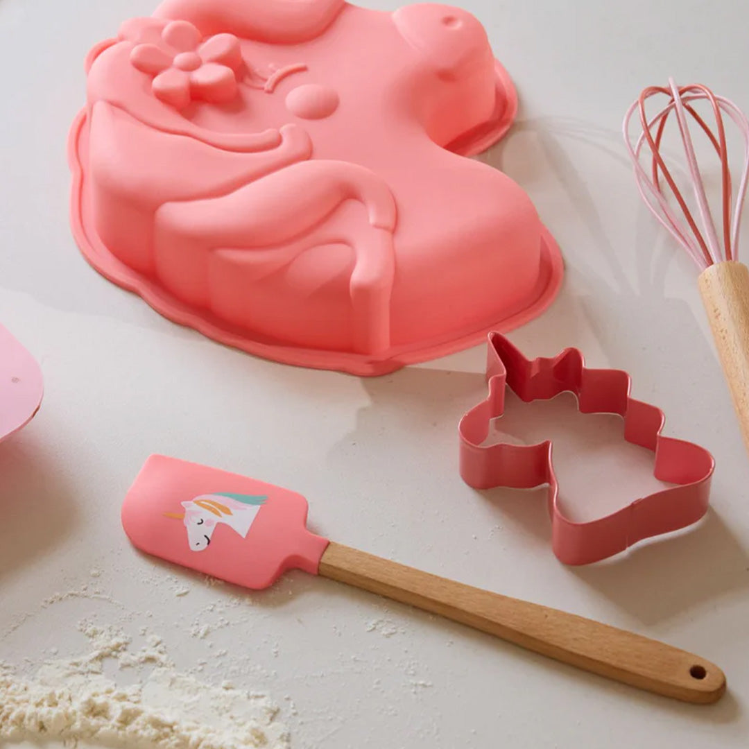 Roze eenhoorn bakset met siliconen bakvorm, uitsteker, garde en spatel op een aanrecht met bloem.