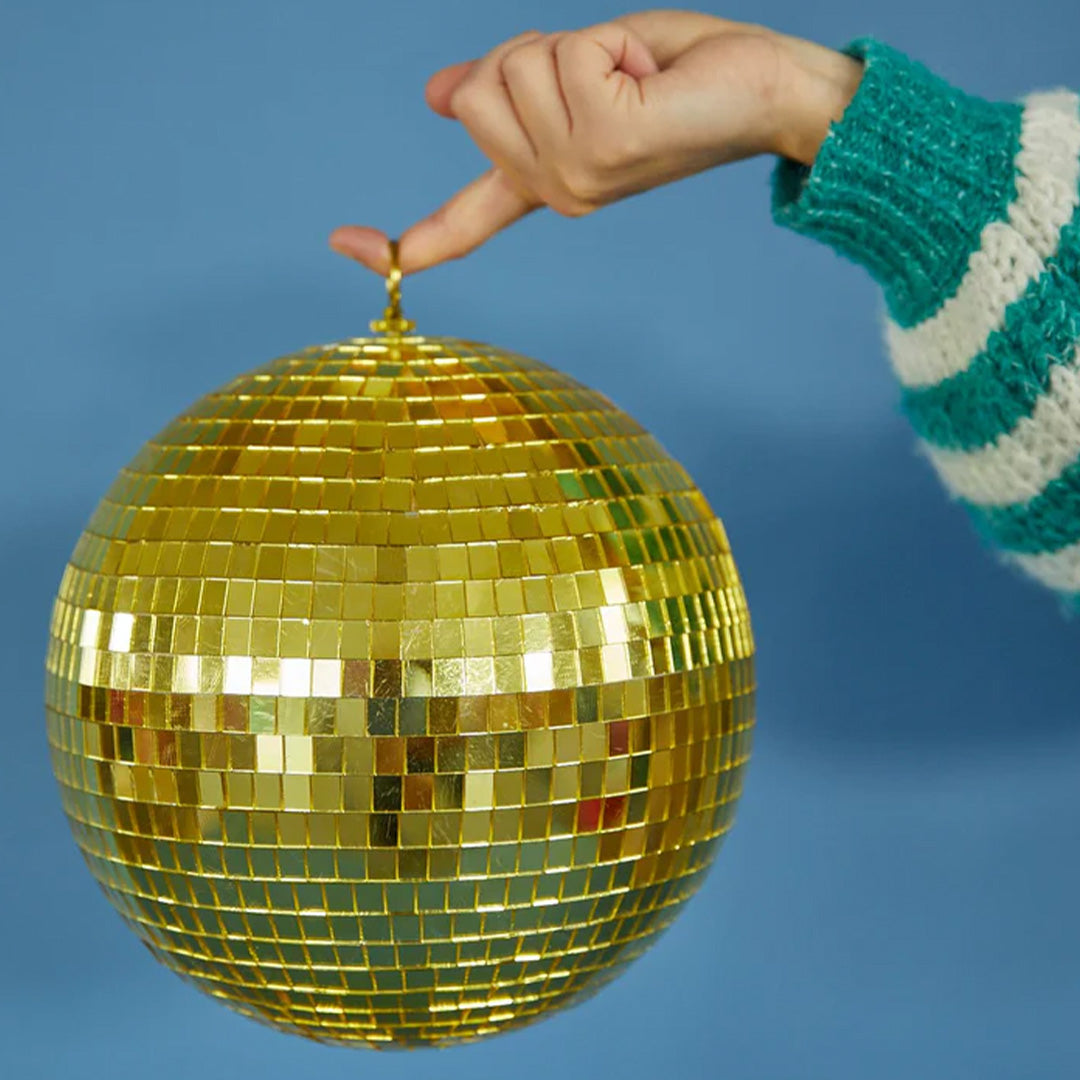 Een hand houdt de Rice gouden discobal van 25 cm vast tegen een blauwe achtergrond.