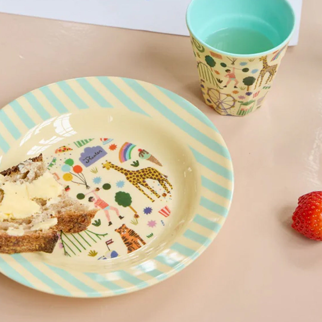 rice kinderkom met brood en boter, naast een bijpassende beker en een aardbei op een roze ondergrond.