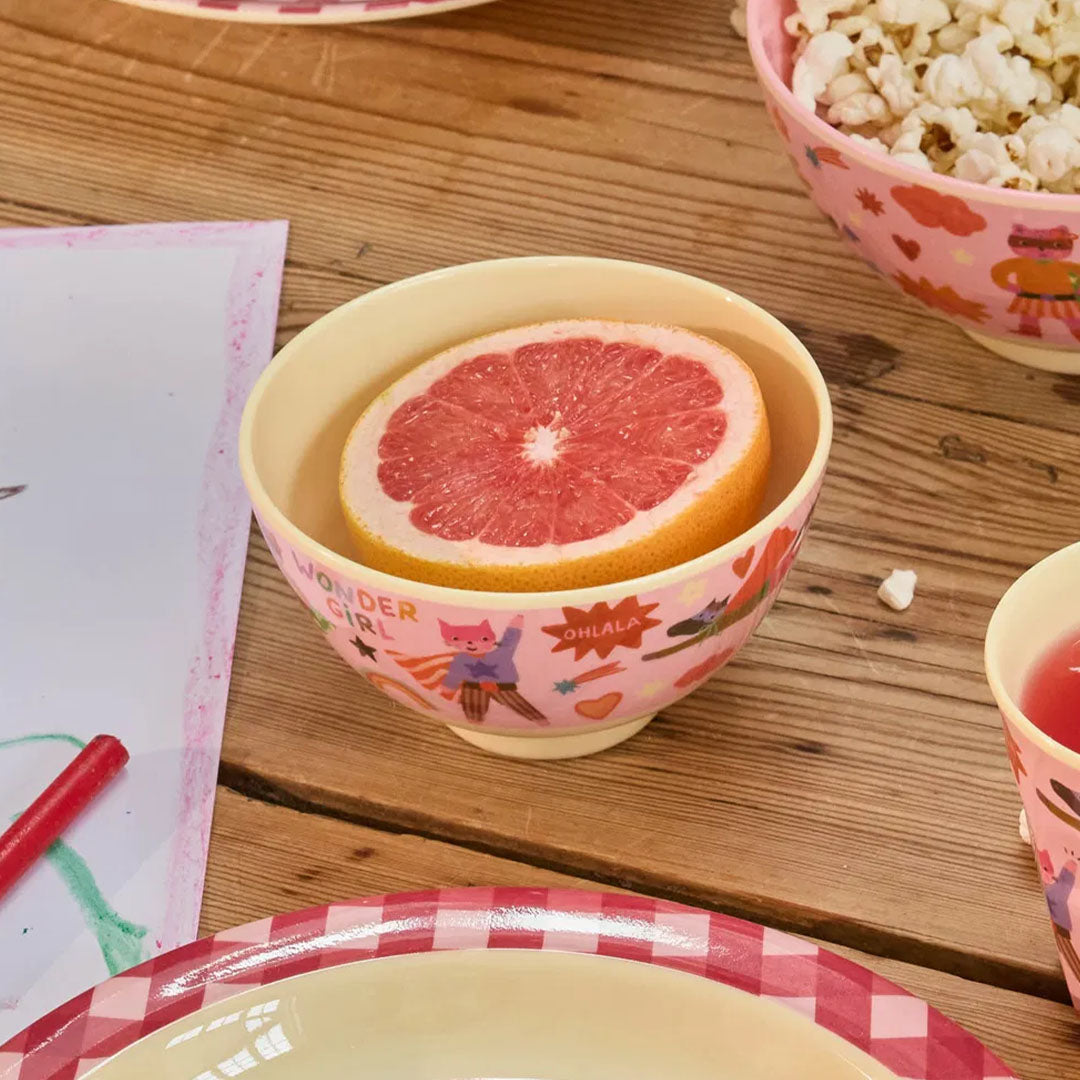 Roze kinderkom met superheldenprint, gevuld met een halve grapefruit, op een houten tafel.