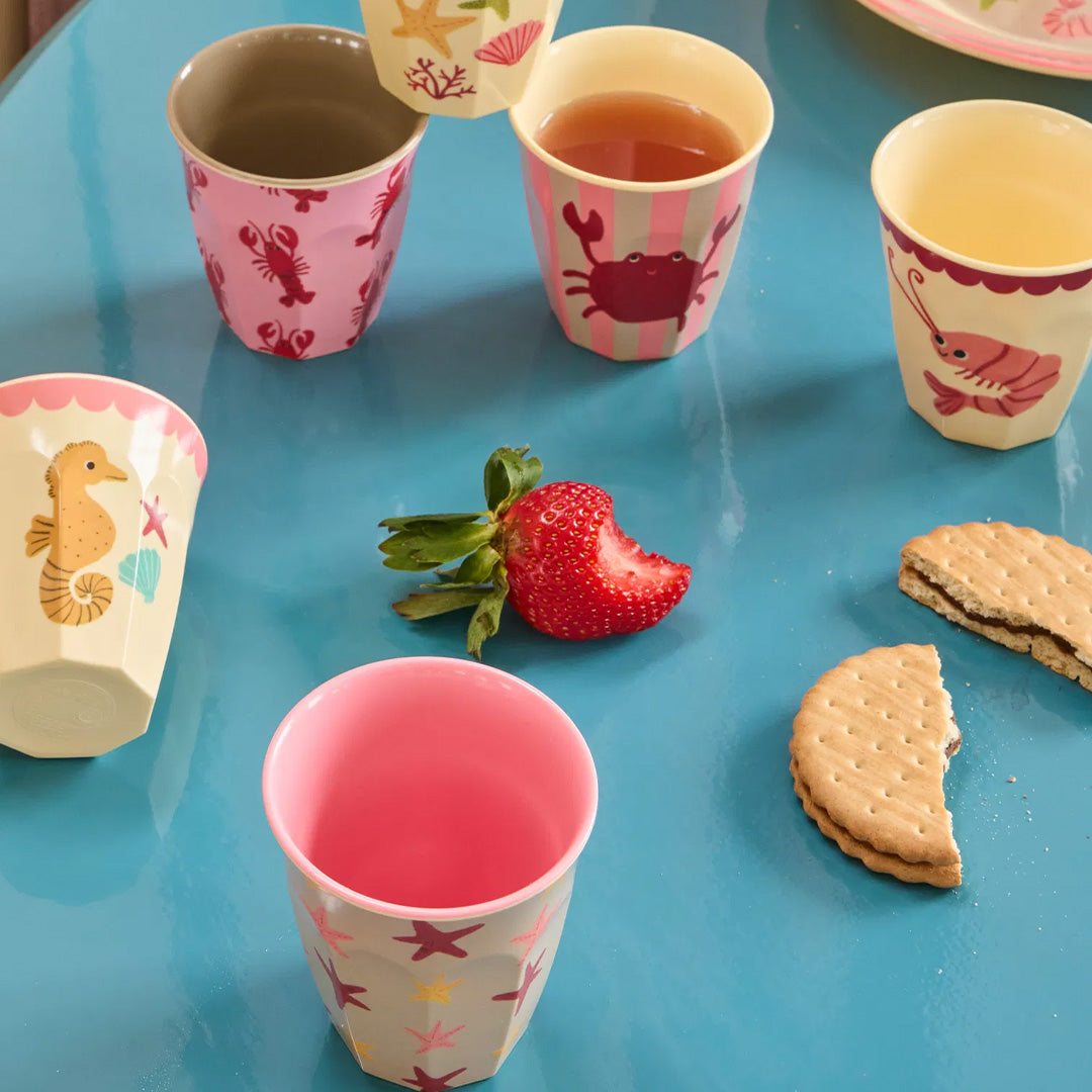 Diverse rice kinderbekers met zeedieren thema op een blauwe tafel, met drankjes, een aardbei en koekjes.