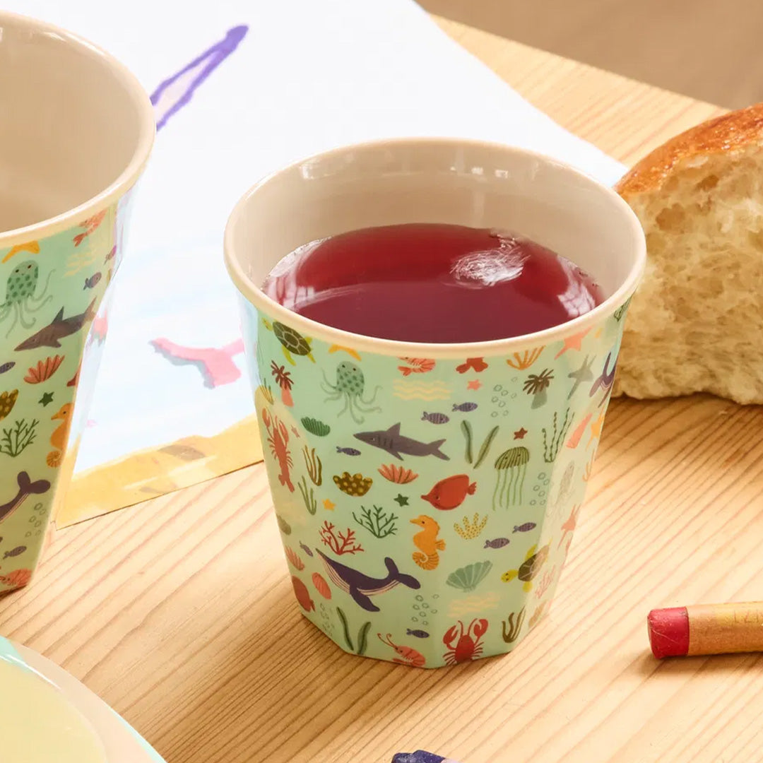Rice kinderbeker met oceaanpatroon gevuld met rode drank op een houten tafel.