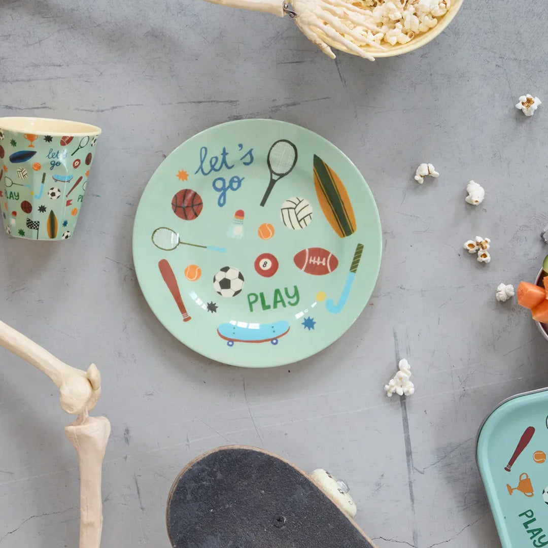 Rice kinderbord met sportthema op een grijze ondergrond, omringd door een bijpassende beker, popcorn en een skateboard.