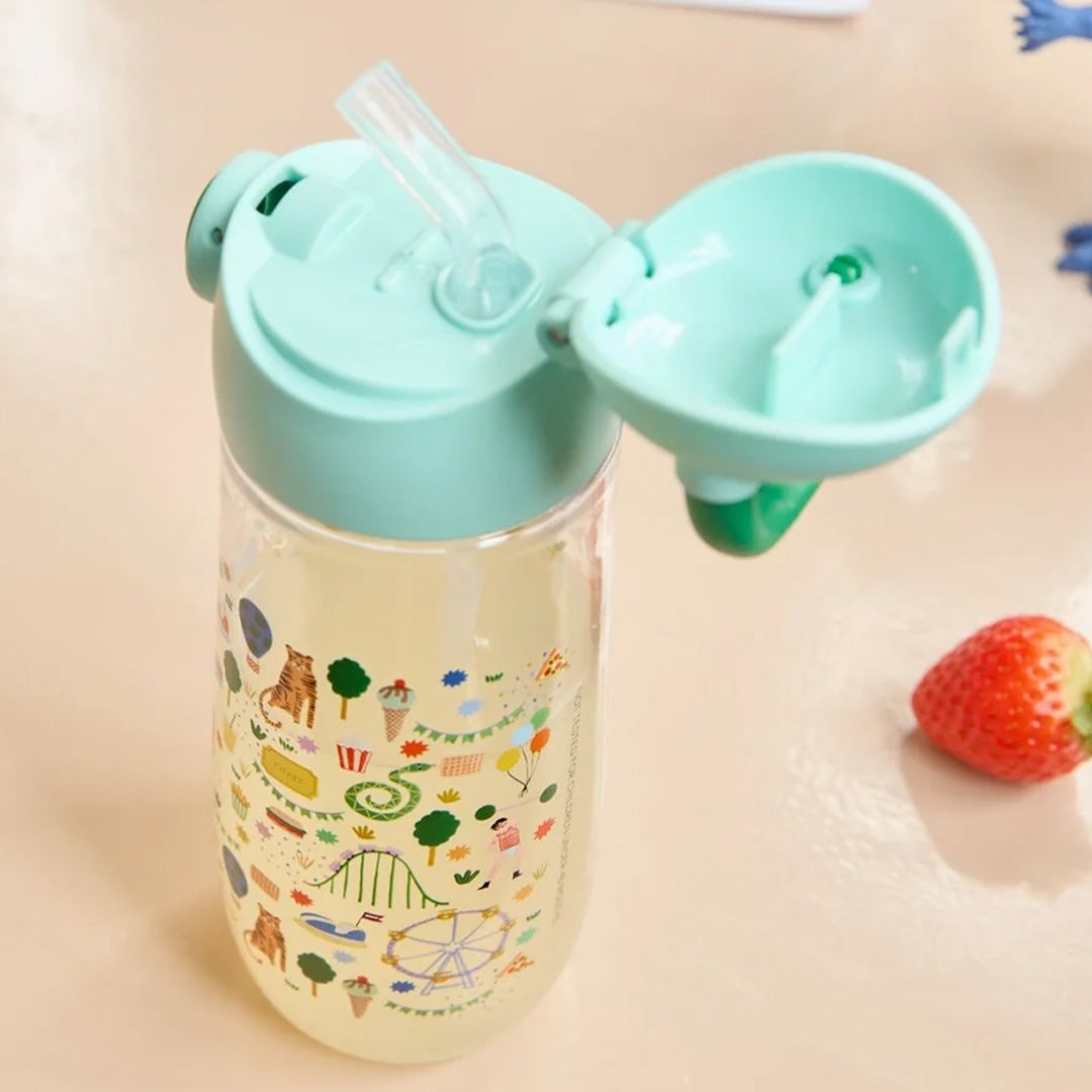 Open rice drinkfles met rietje en kermisfiguren, gevuld met een gele drank.