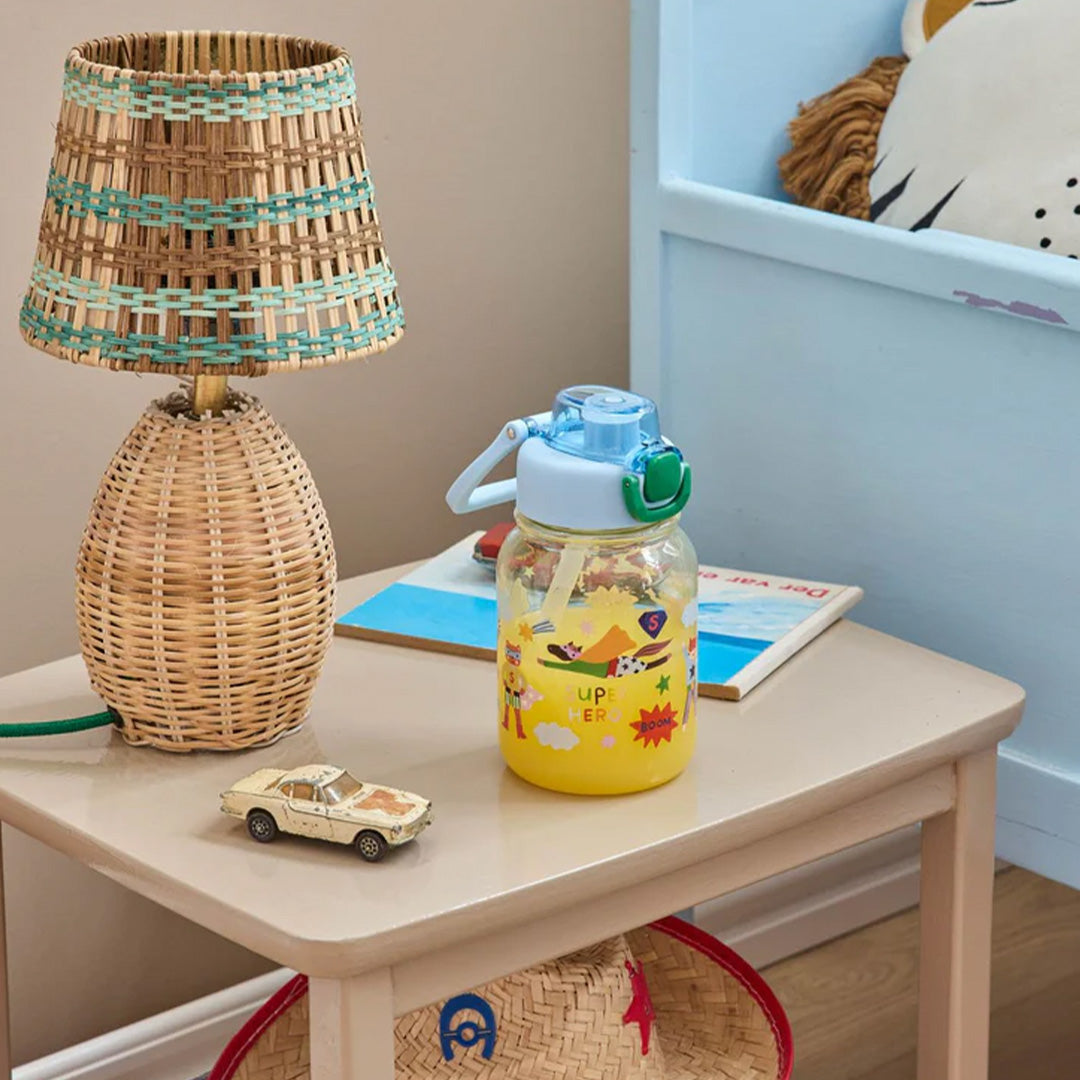 rice kinderdrinkfles met superheldenprint gevuld met gele drank op een nachtkastje.
