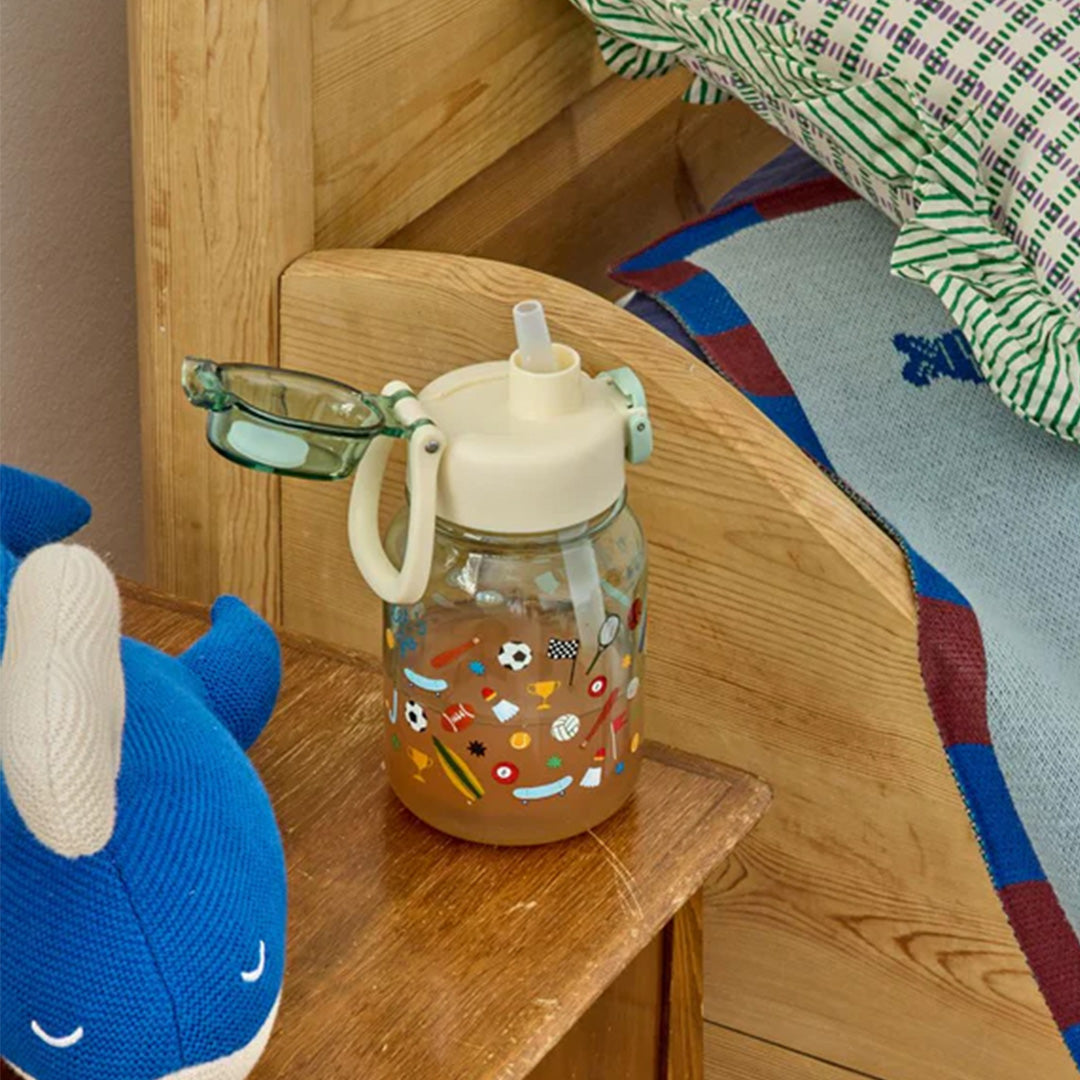 rice drinkfles sports met sportillustraties op een houten nachtkastje naast een blauwe knuffel.