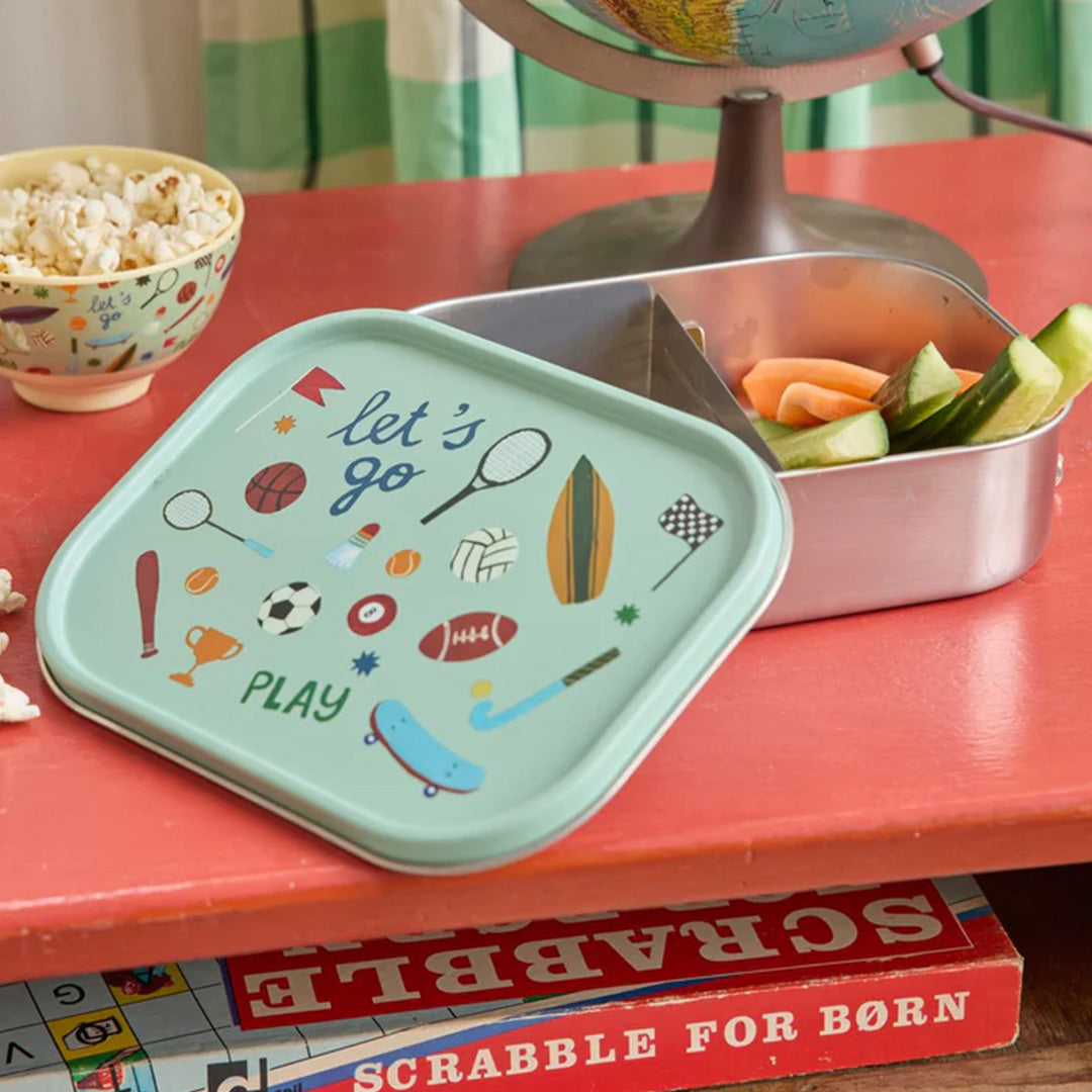 rice rvs broodtrommel met sportthema deksel op een rode tafel, gevuld met komkommer en wortel.