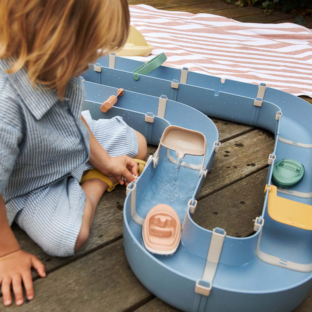 Kind speelt met de Liewood waterbaan op een houten terras, water stroomt door de baan.
