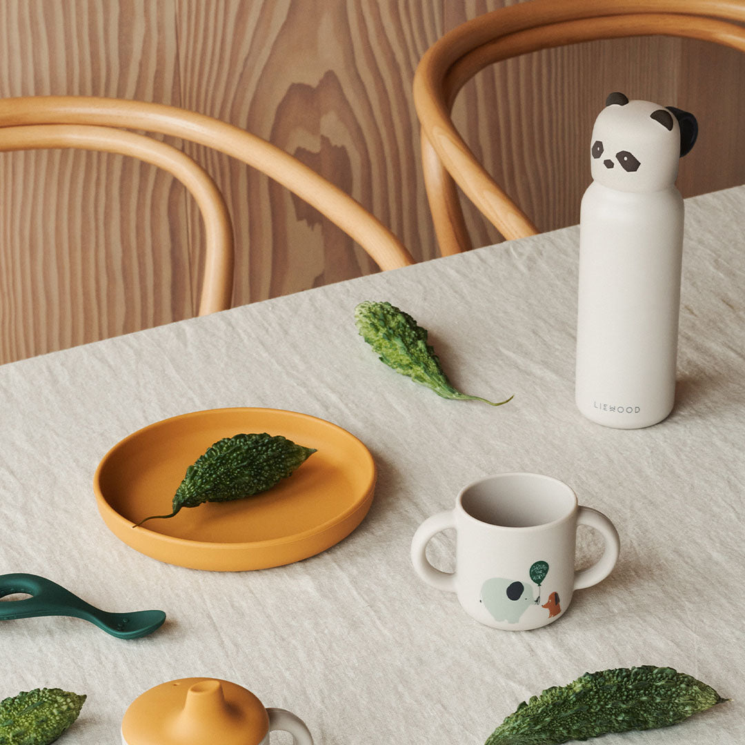 Liewood kinder serviesgoed op een tafel, met de beige panda thermosfles, een gele bord en een beker.