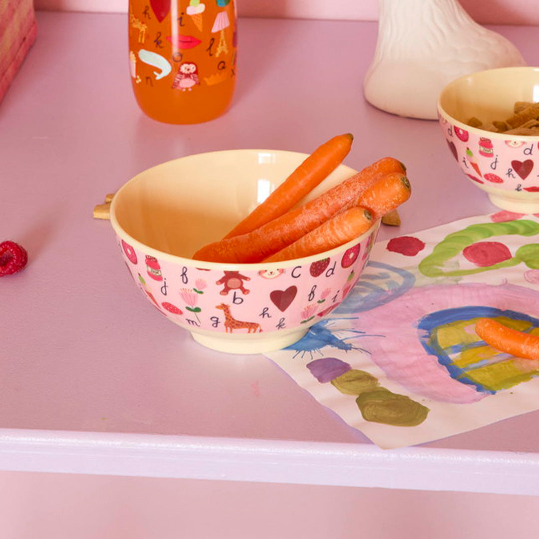 Roze kinderkom met ABC-figuren gevuld met wortels op een roze tafel.