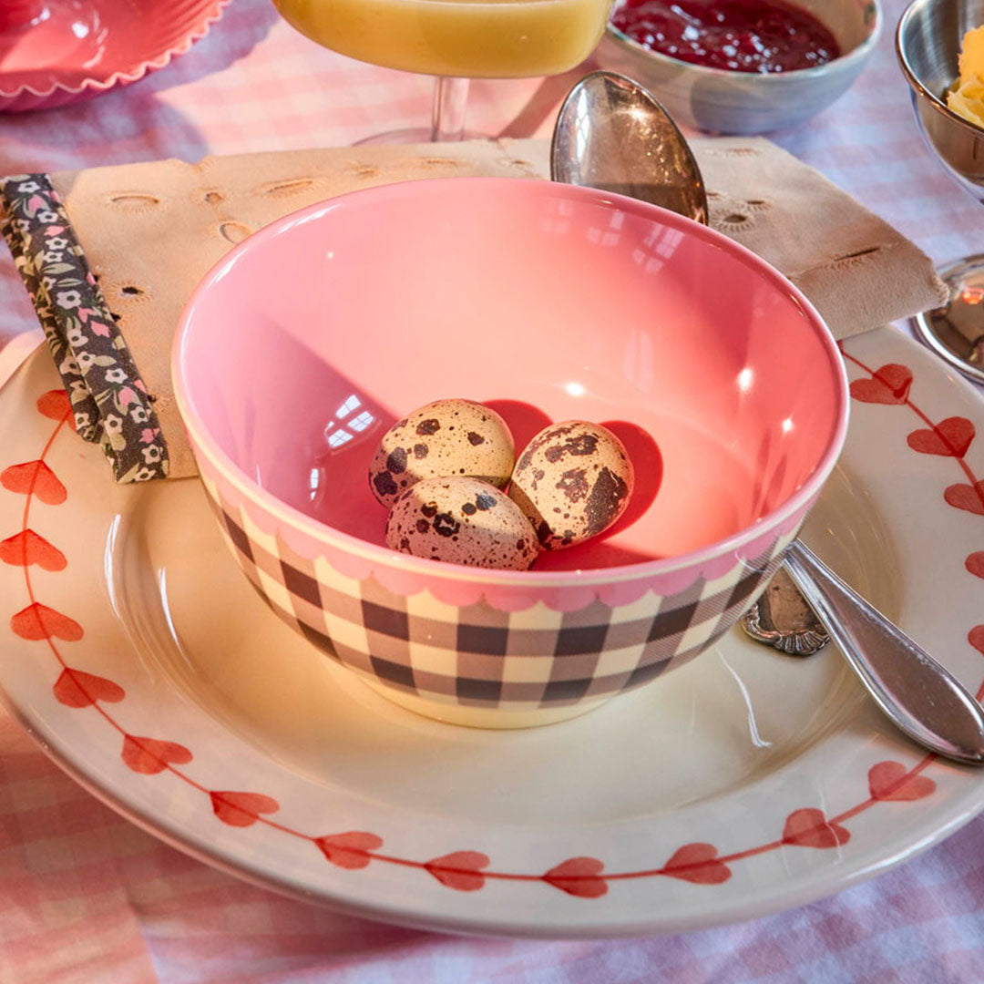 rice kinderkom met geruit patroon en roze binnenkant, gevuld met kwarteleitjes op een ontbijttafel.