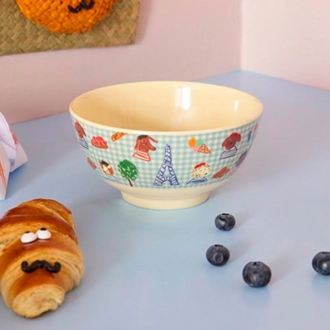 Rice kinderkom met Parijs-thema, staand op een blauwe ondergrond naast een croissant en blauwe bessen.