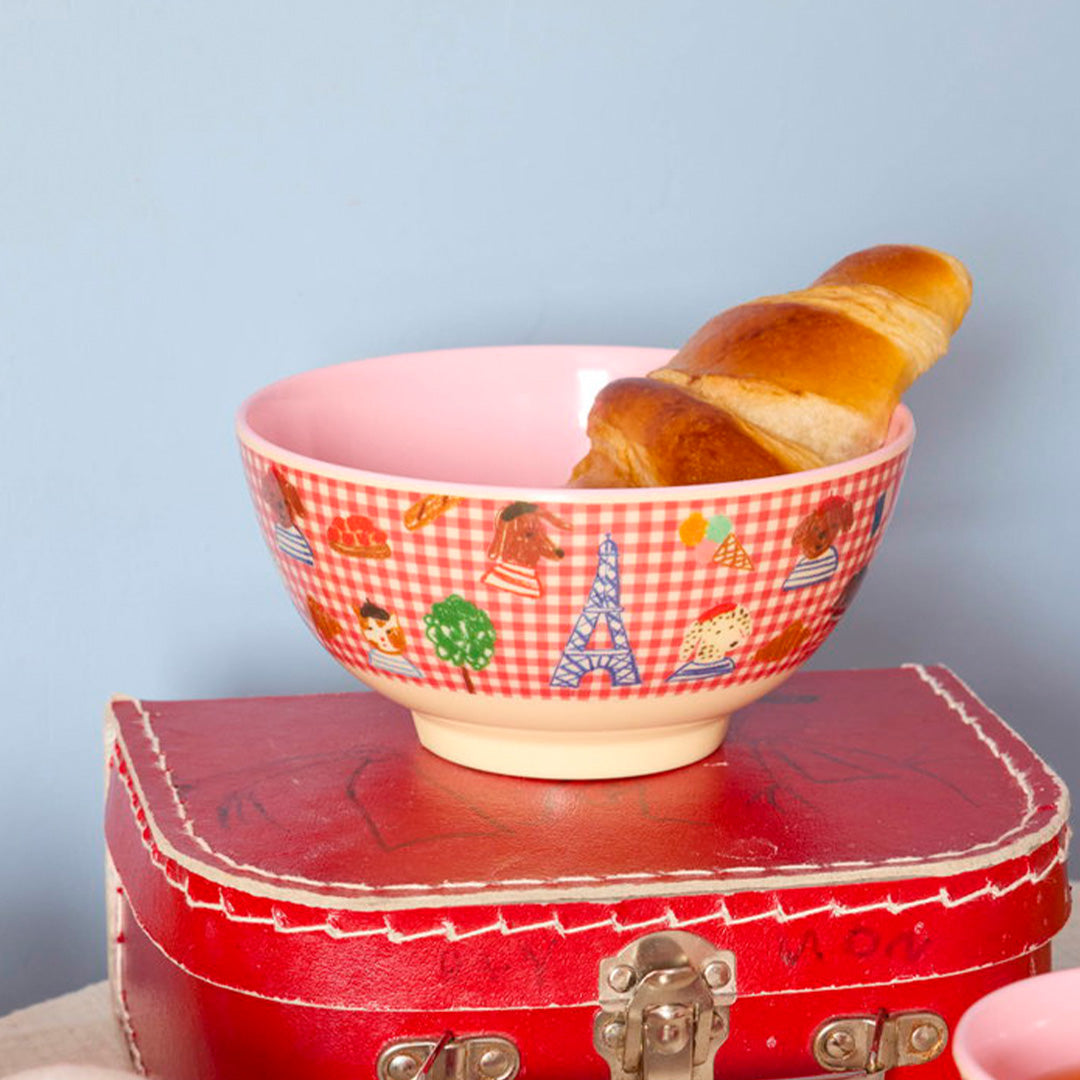 rice kinderkom met 'Kids in Paris' thema en een croissant erin, staand op een rode koffer.