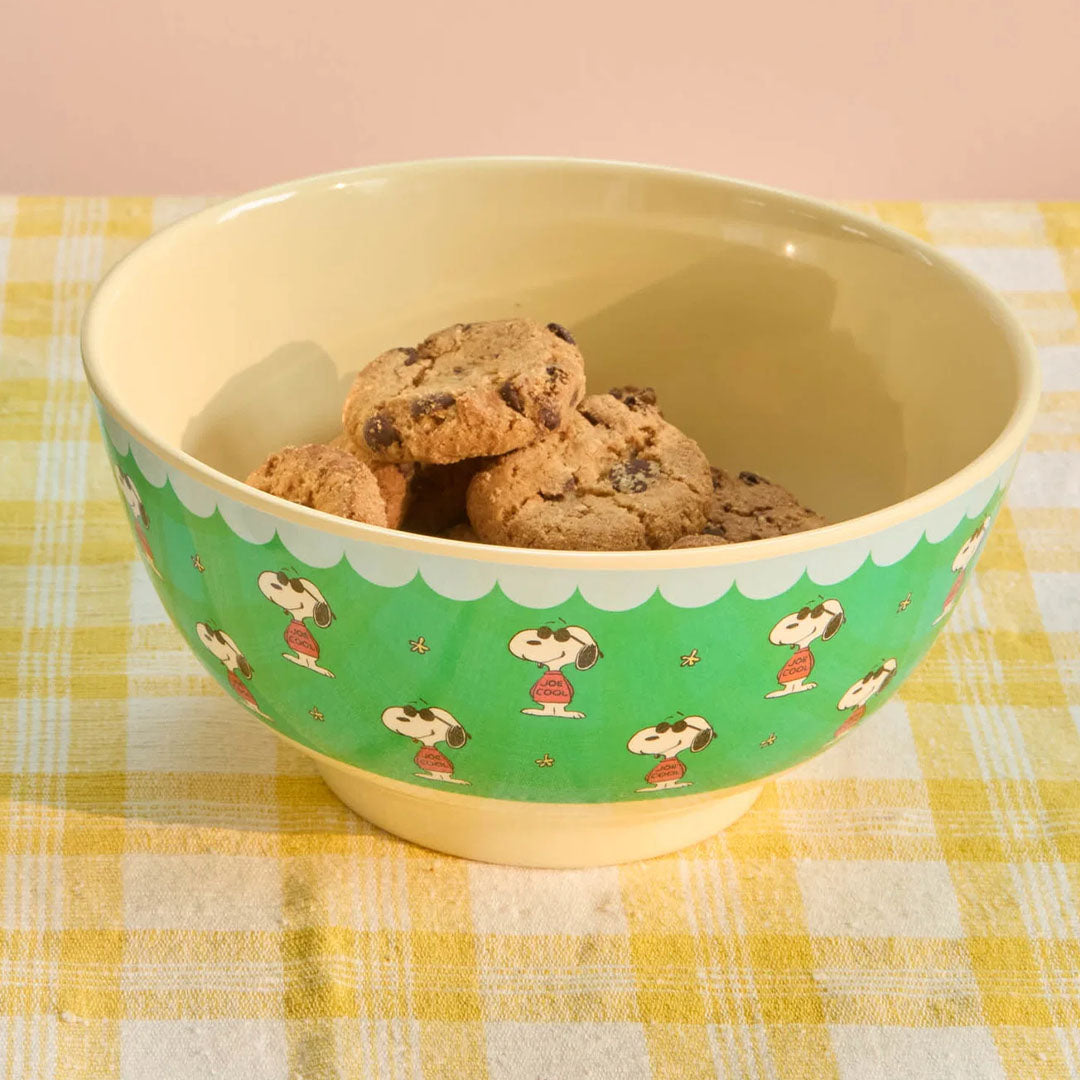 Een Rice kinderkom met Snoopy figuren, gevuld met koekjes op een geel geruite ondergrond.