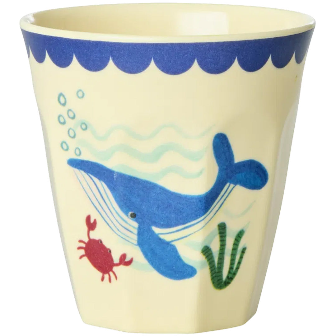 Een Rice kinderbeker met een blauwe walvis, rode krab en groene planten op een beige achtergrond.