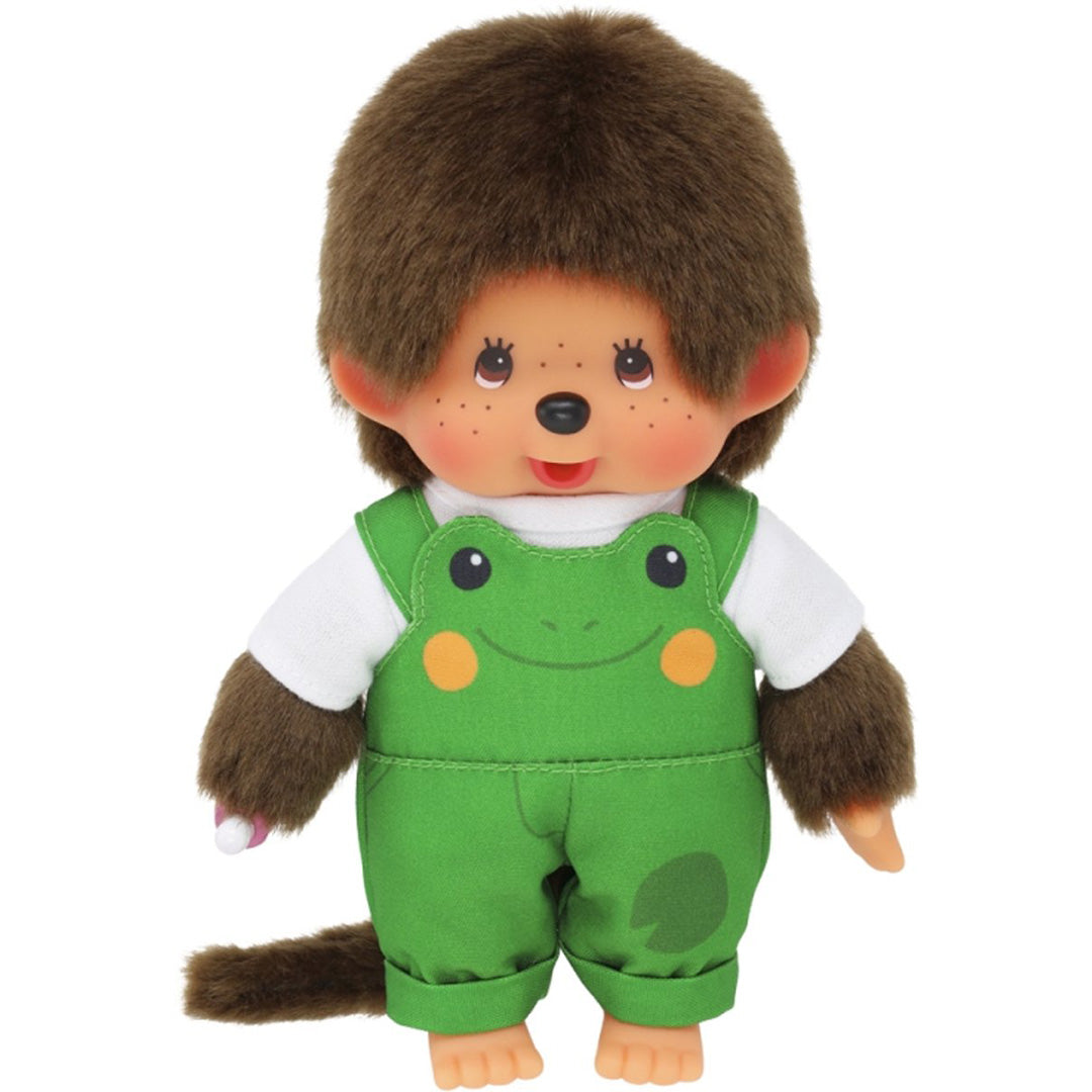 Monchhichi pop jongen met bruin haar en een groene kikker tuinbroek, met een roze speen in de hand.