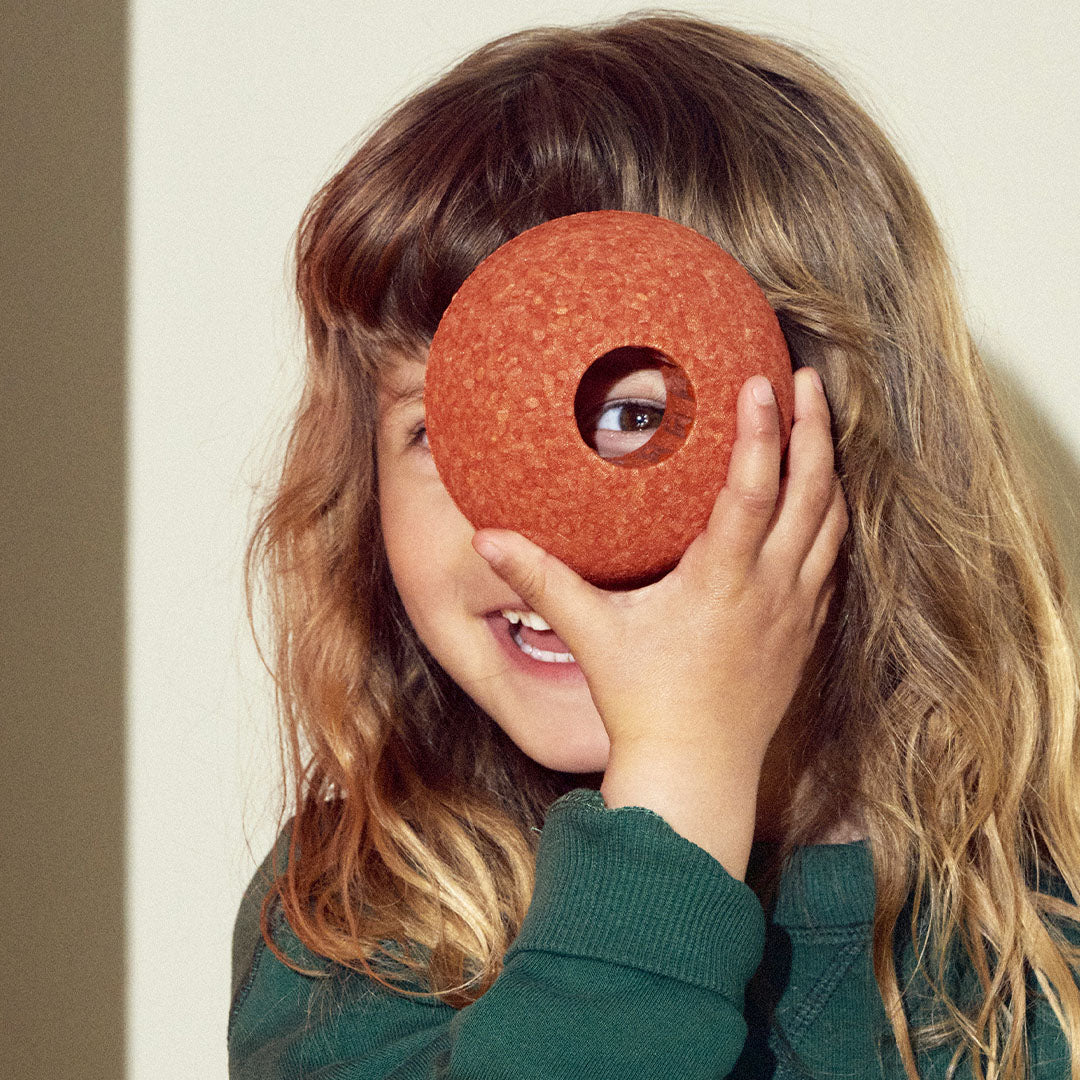 Een kind kijkt door het gat van een Modu burnt orange schuimrubber halve bal.