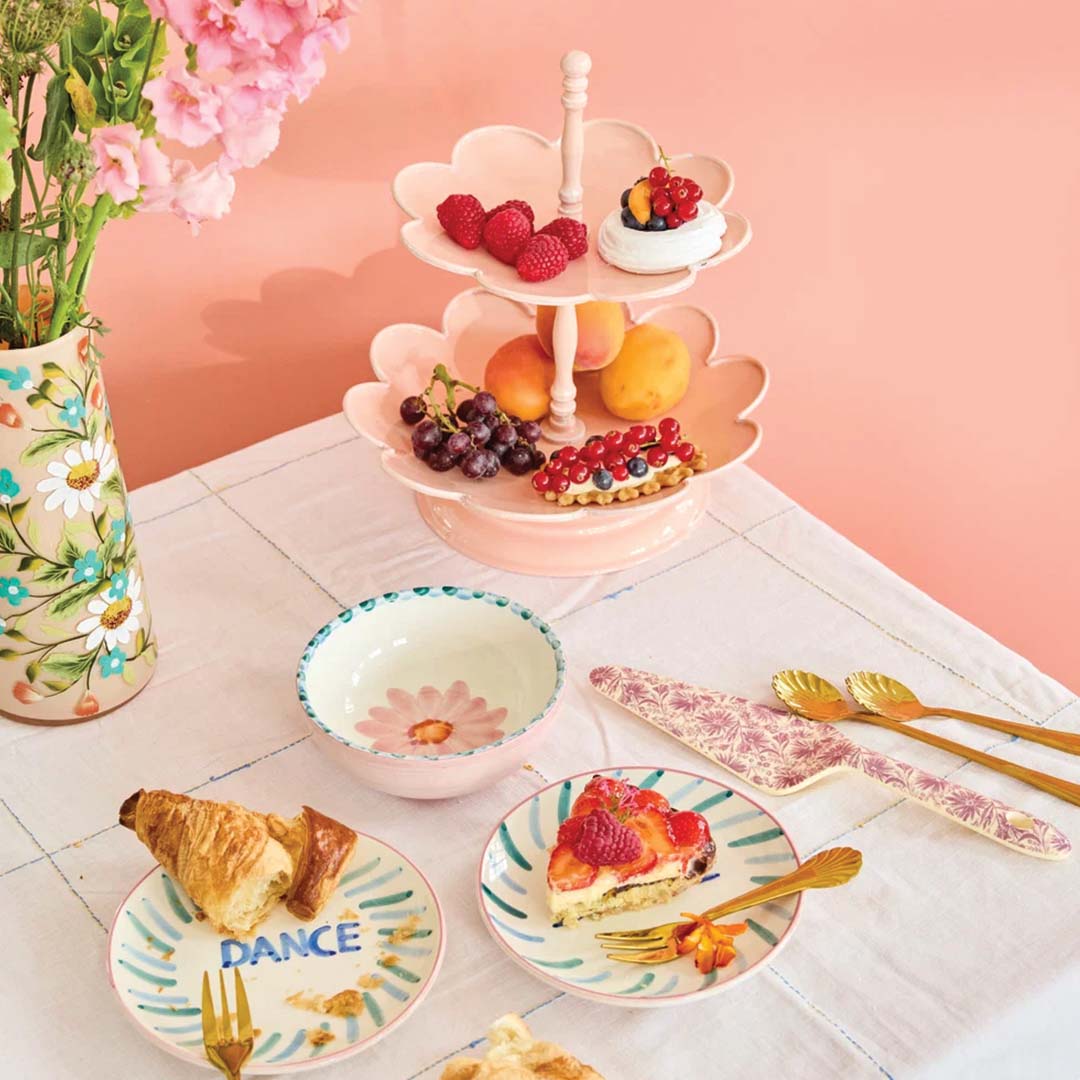 De roze rice etagère met bloemvormige lagen gevuld met fruit en gebak op een gedekte tafel.