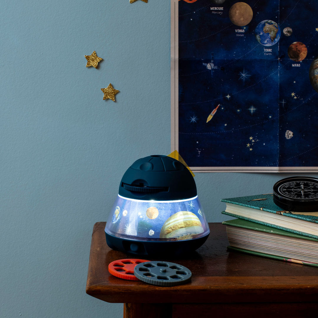 De Moulin Roty ruimteprojector staat op een nachtkastje en verlicht een muur met een ruimteposter.