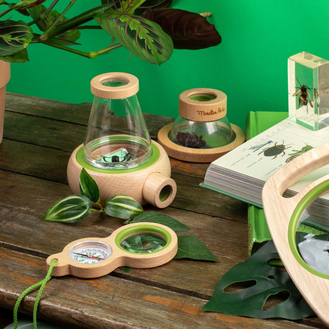 Moulin Roty houten vergrootglas met kompas op een houten tafel, omringd door andere natuur ontdekkingssets en planten.