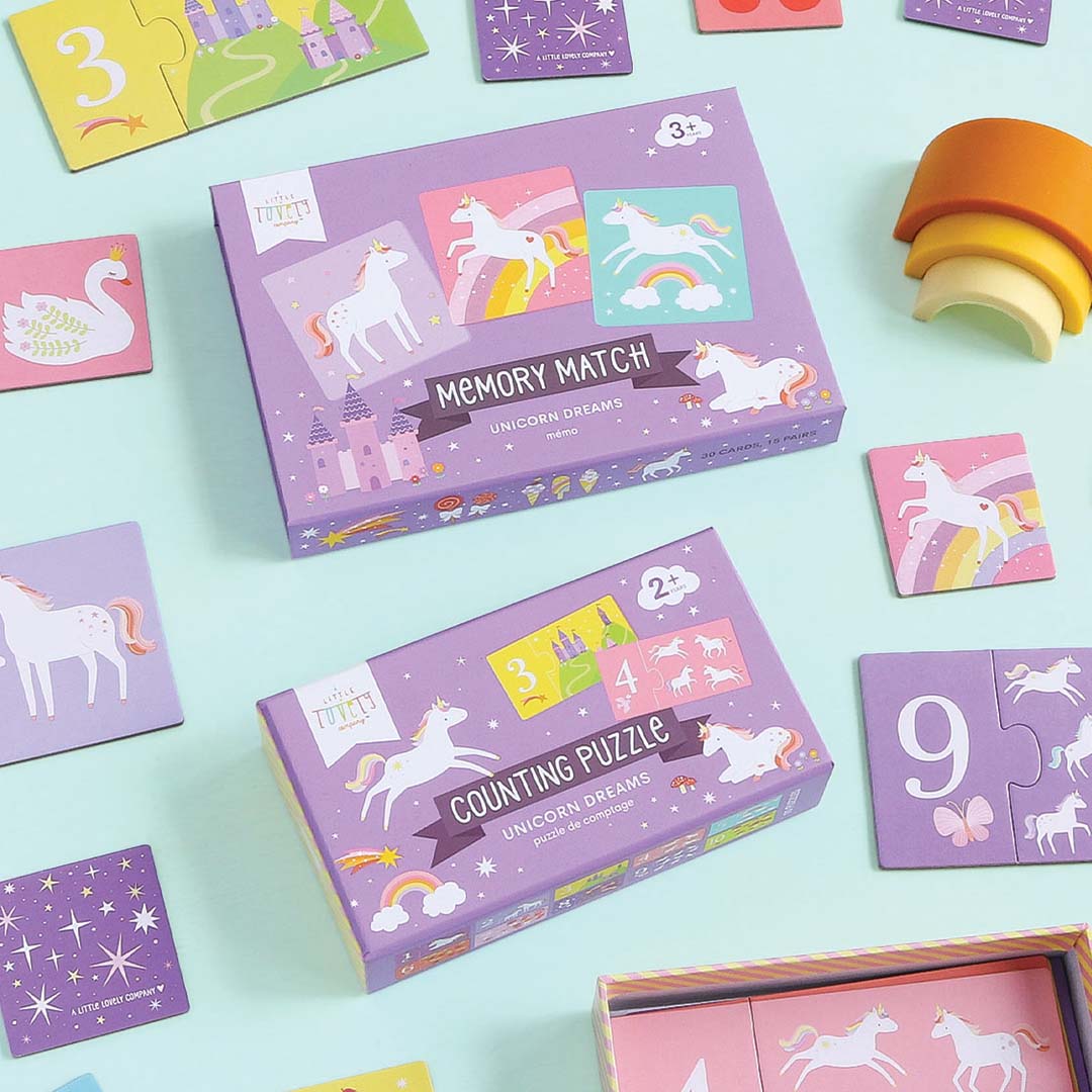 Twee paarse A Little Lovely Company speelgoeddozen, een Unicorn Dreams memory en een telpuzzel, omringd door losse speelkaarten.