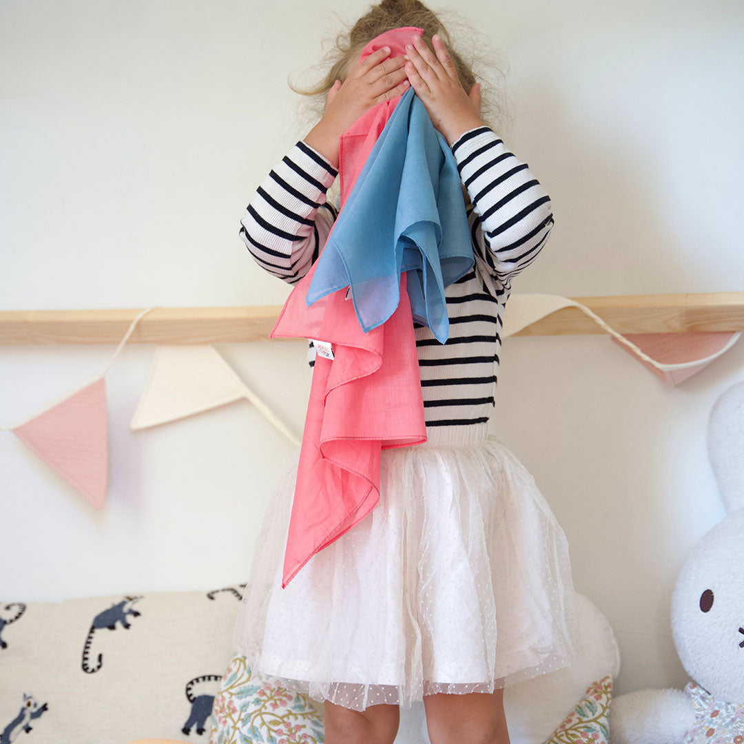 Een kind speelt kiekeboe met een blauw en een roze pit and play speeldoek.