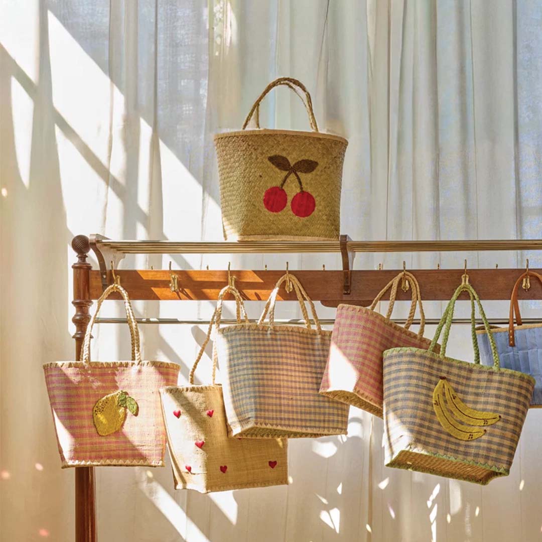 Collectie rice kindertassen van raffia met diverse patronen hangend aan een houten rek.