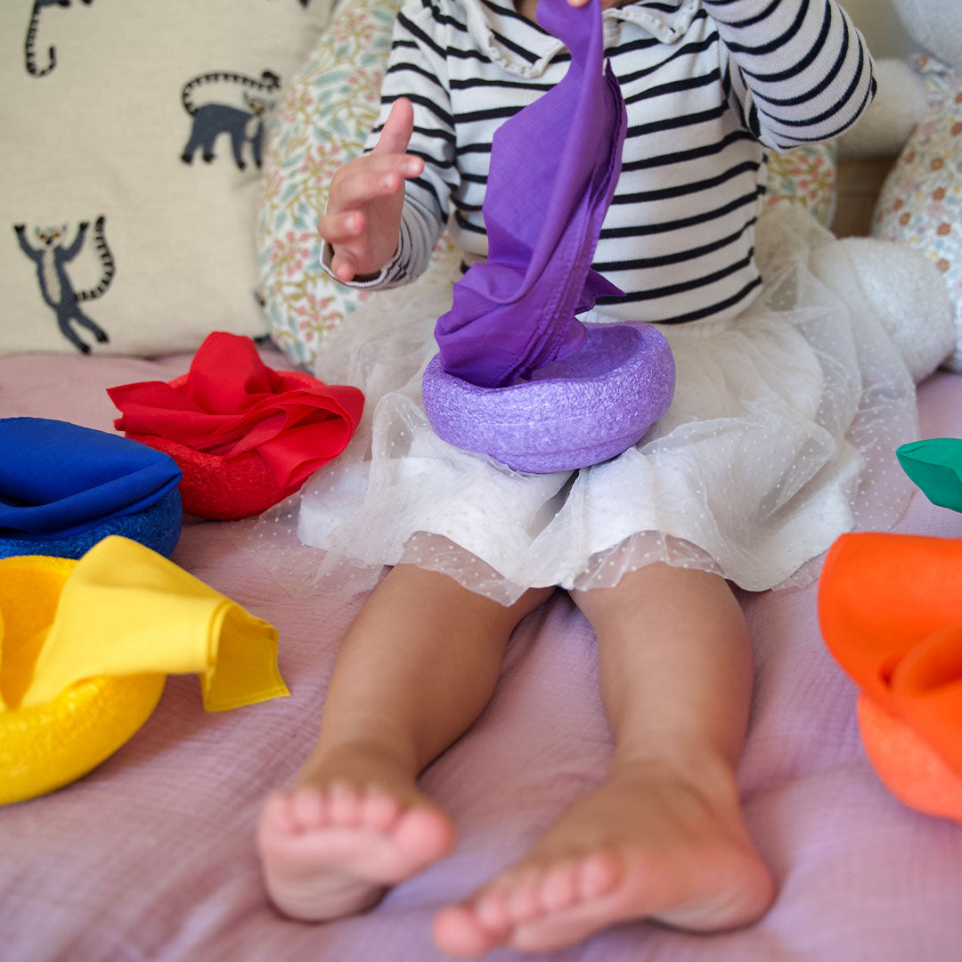 Kind stopt een paarse pit and play speeldoek in een paarse vilten schaal.