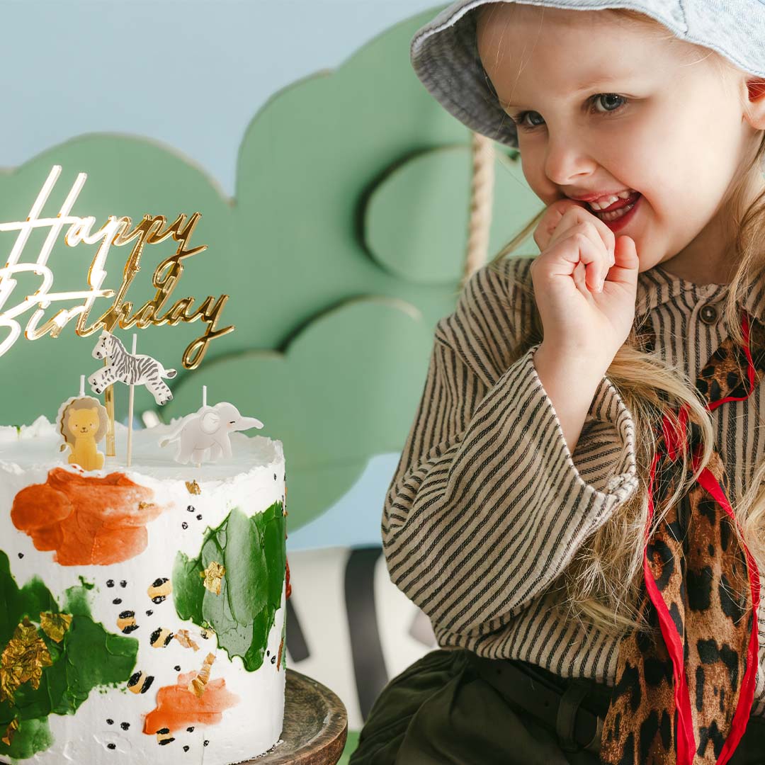 Een lachend meisje kijkt naar een verjaardagstaart met de Partydeco safari dieren kaarsjes en een 'Happy Birthday' topper.
