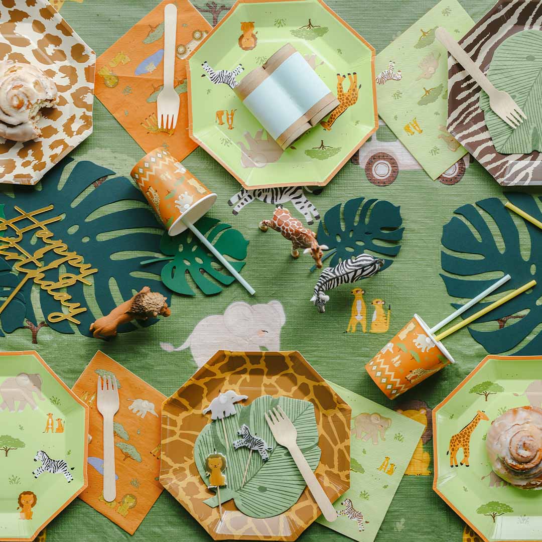 PartyDeco safari feestartikelen met borden, servetten, bekers, bestek en speelgoed dieren op een groene tafel.