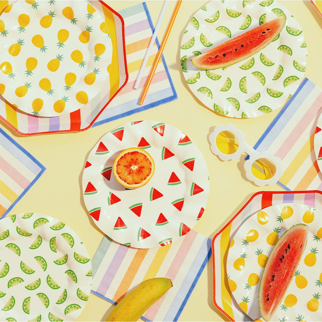 Partydeco collectie feestartikelen met zomerfruitpatronen en gestreepte servetten, samen met echt fruit en een zonnebril.