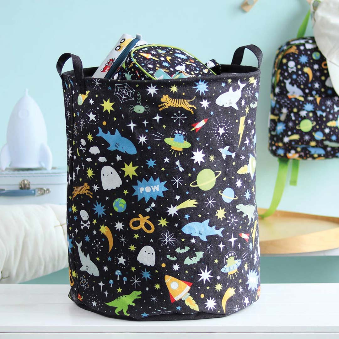 A Little Lovely Company opbergmand met galaxy print, gevuld met spullen, staand op een witte plank in een kinderkamer.