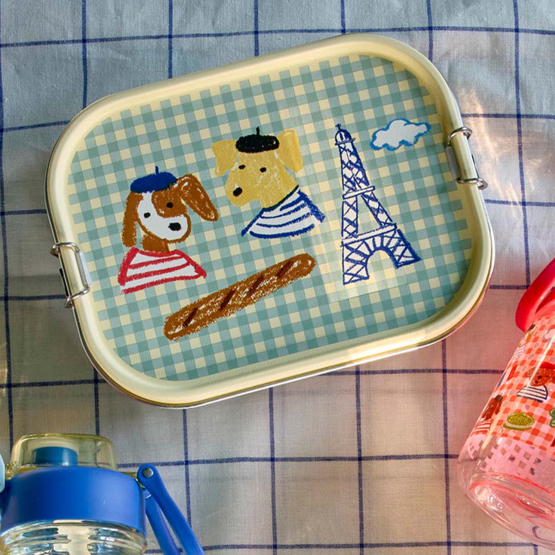 rice rvs broodtrommel voor kinderen met een geruit patroon en Parijs-thema, liggend op een geruite ondergrond naast drinkflessen.