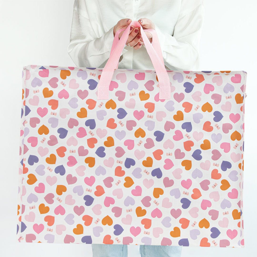 Een persoon houdt een a little lovely company opbergtas met veelkleurige hartjespatroon vast.