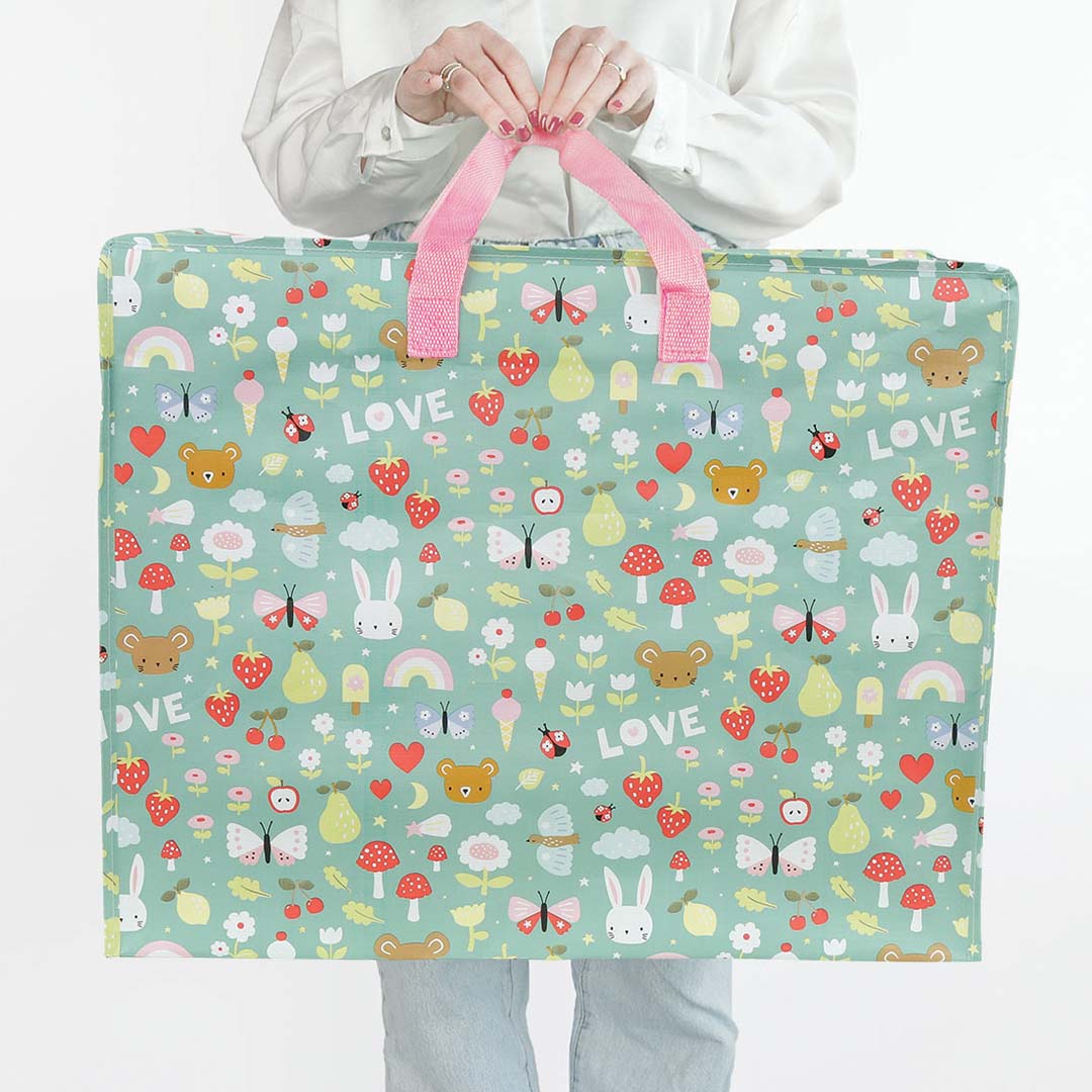 Een persoon houdt de a little lovely company XL opbergtas met groen dieren- en regenboogpatroon voor zich uit.
