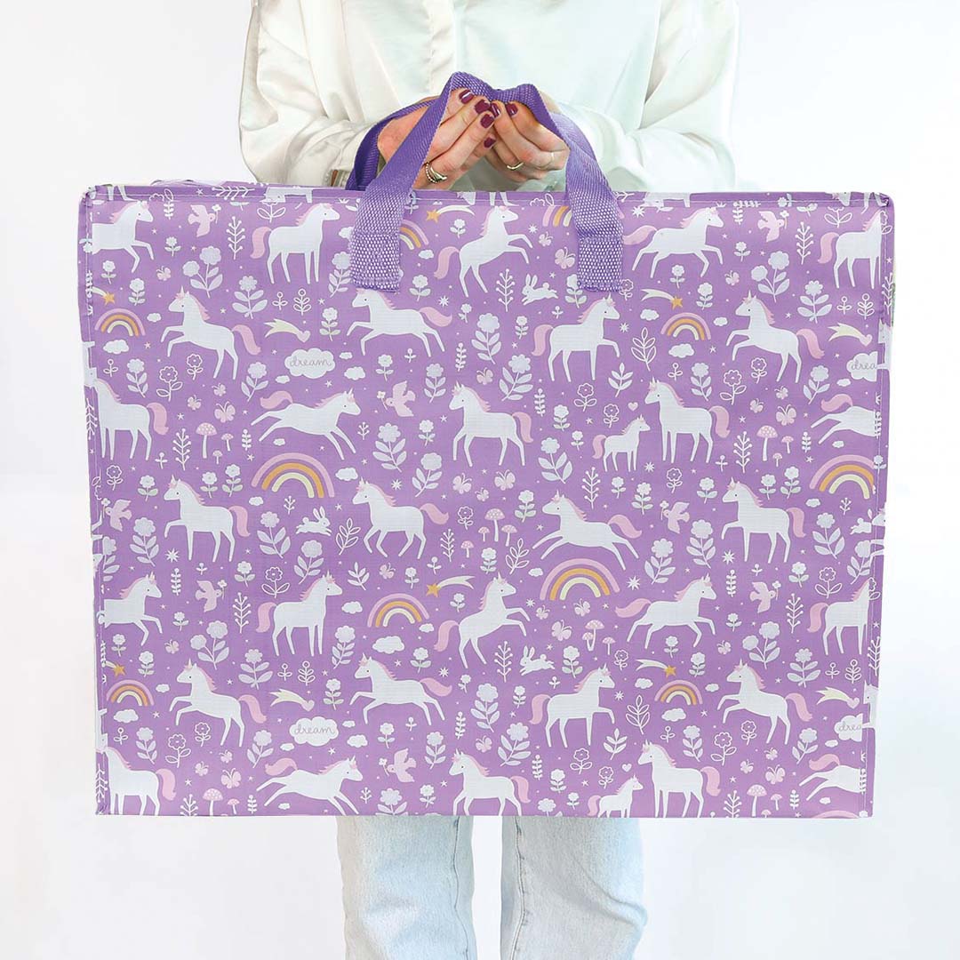 Een persoon houdt de a little lovely company XL opbergtas met eenhoornprint vast om de grootte te tonen.