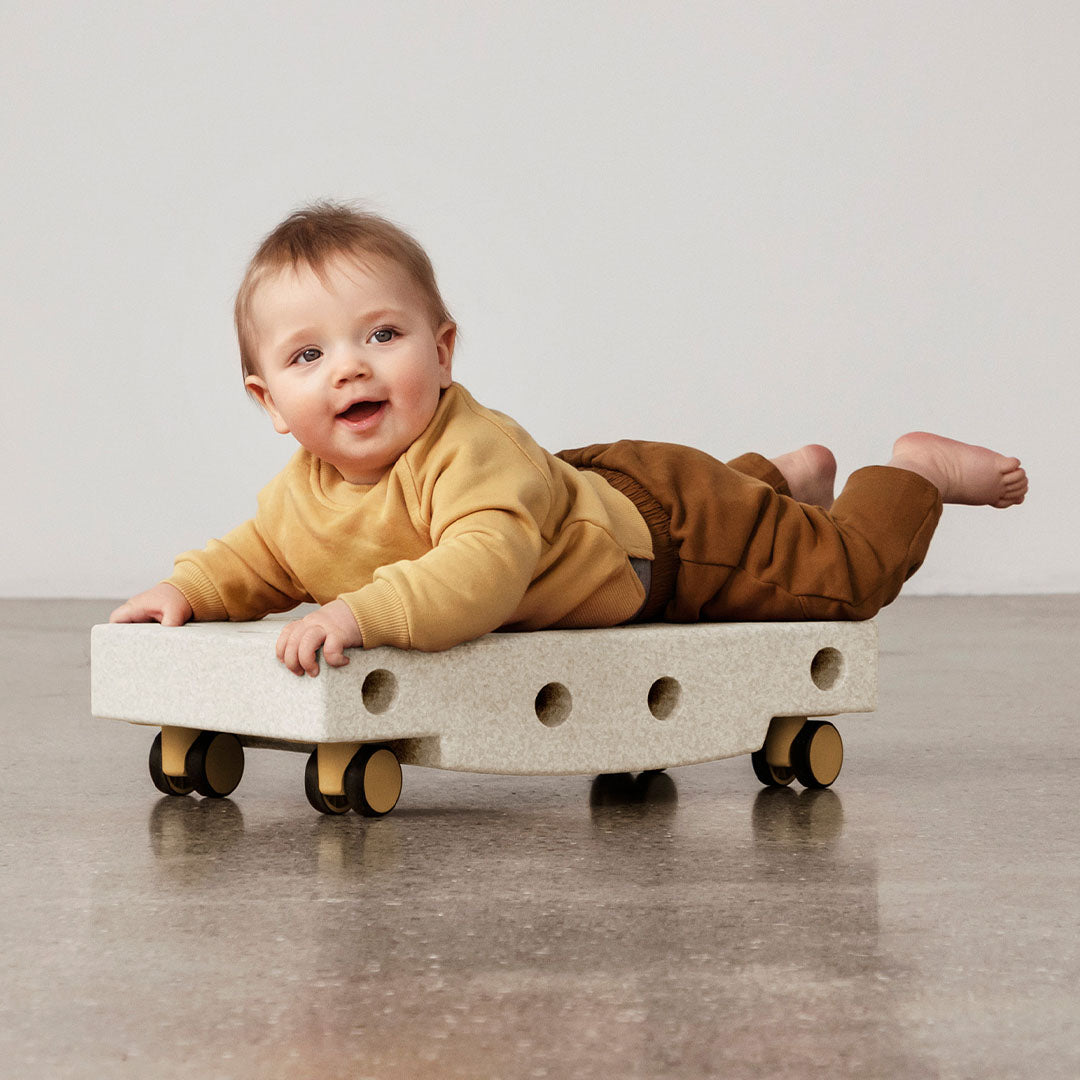 Een lachende baby ligt op zijn buik op een modu schuimrubberblok dat is opgebouwd als rijdend speelgoed.