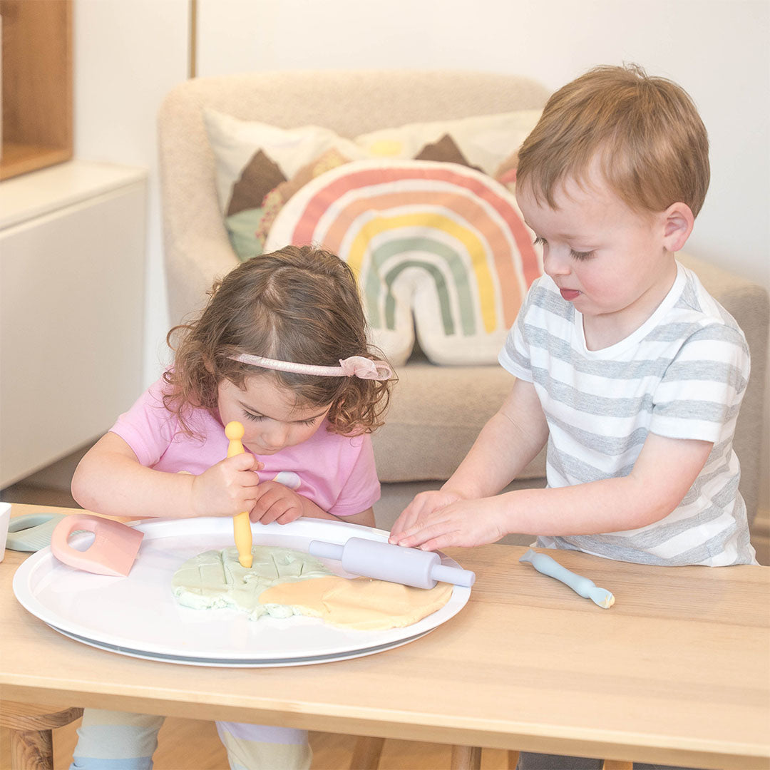 Twee kinderen spelen met klei en de Inspire My Play siliconen klei-accessoires aan een houten tafel.