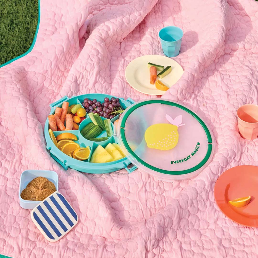 rice snackbox met 6 vakken gevuld met fruit en groenten op een roze picknickkleed.