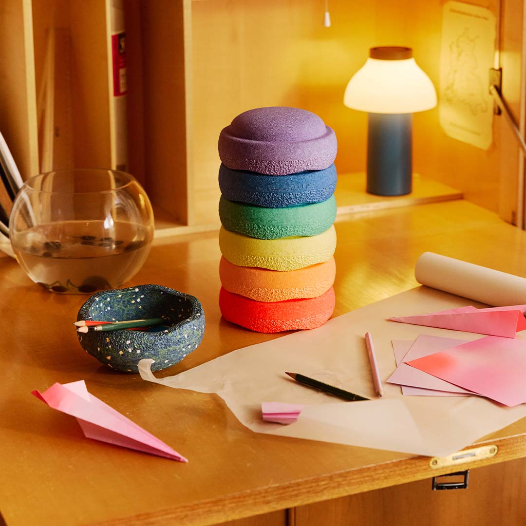 stapelstein regenboog stapelblokken op een bureau met knutselspullen en een lamp.