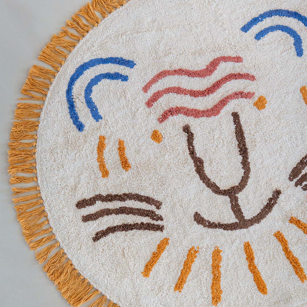 Close-up van een deel van het ronde vloerkleed met leeuwenkop en franjes.
